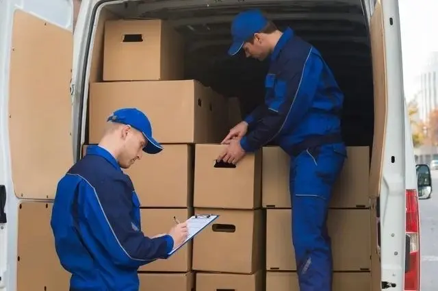 Two men in blue work clothes loading boxes into a truck.